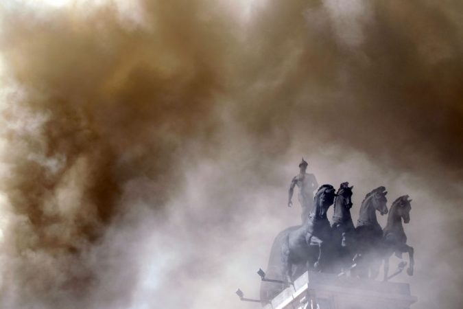 El humo de un incendio tapa el auriga del antiguo edificio del Banco de Bilbao que simboliza al capital financiero guiando las cuatro grandes industrias del país.